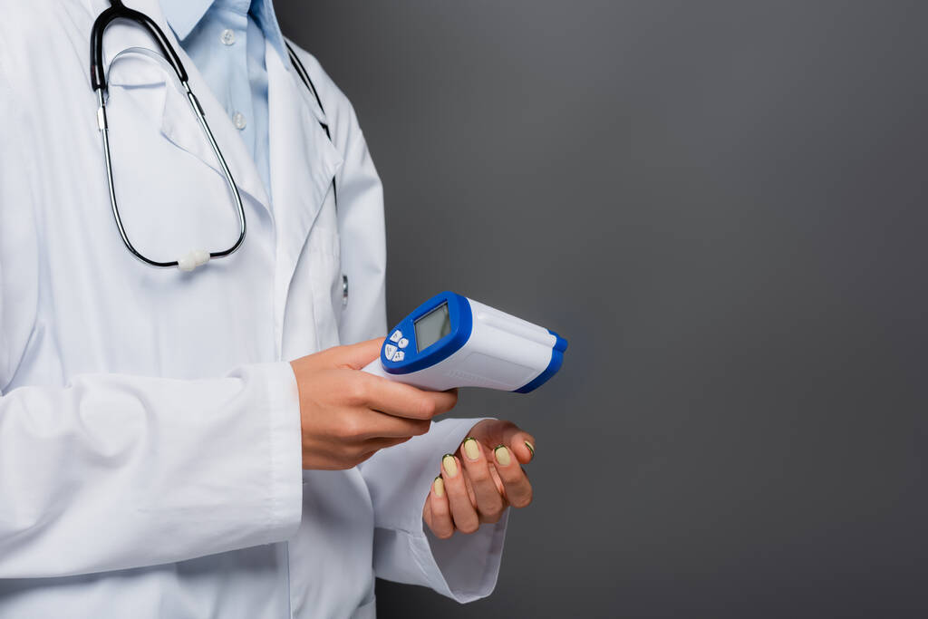 Vista recortada del médico que sostiene pirómetro sin contacto aislado en gris  - Foto, imagen