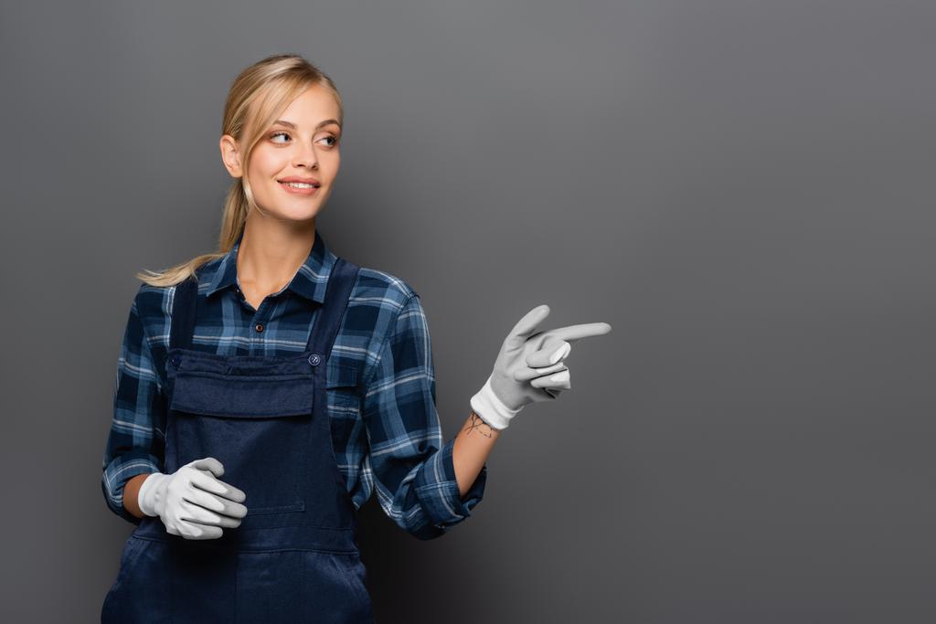 Улыбающийся сантехник в перчатках, указывающий пальцем на серый  - Фото, изображение