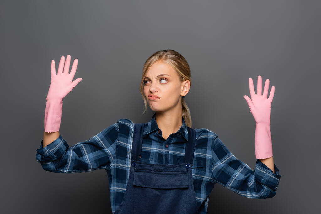 Нечистий сантехнік в комбінезоні дивиться на руки в гумових рукавичках ізольовані на сірому
  - Фото, зображення