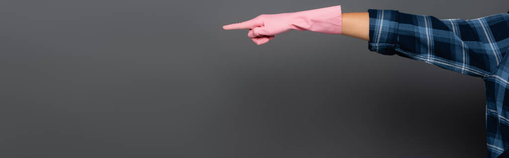 Обрезанный вид водопроводчика в клетчатой рубашке и резиновой перчатке, указывающий пальцем на серый, баннер  - Фото, изображение