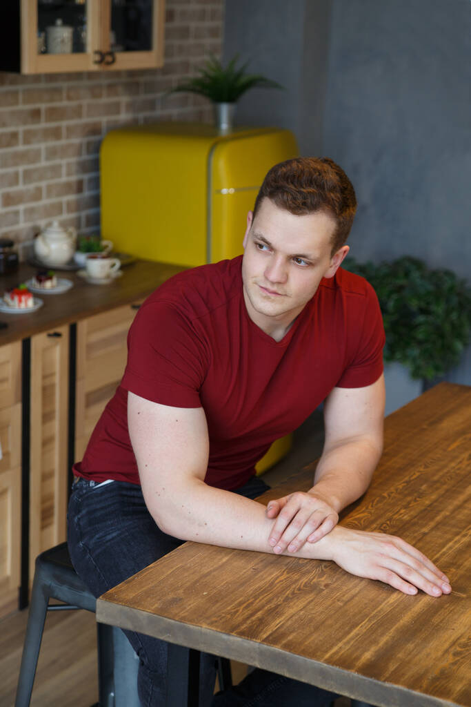 Молодой привлекательный парень сидит в интерьере уютной кухни. - Фото, изображение