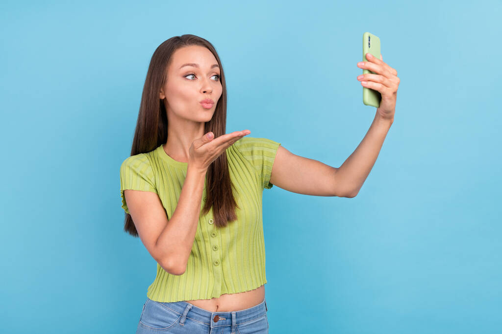 Fénykép flört boldog pozitív fiatal nő tartsa telefon, hogy szelfi küld pálma levegő csók elszigetelt kék színű háttér. - Fotó, kép