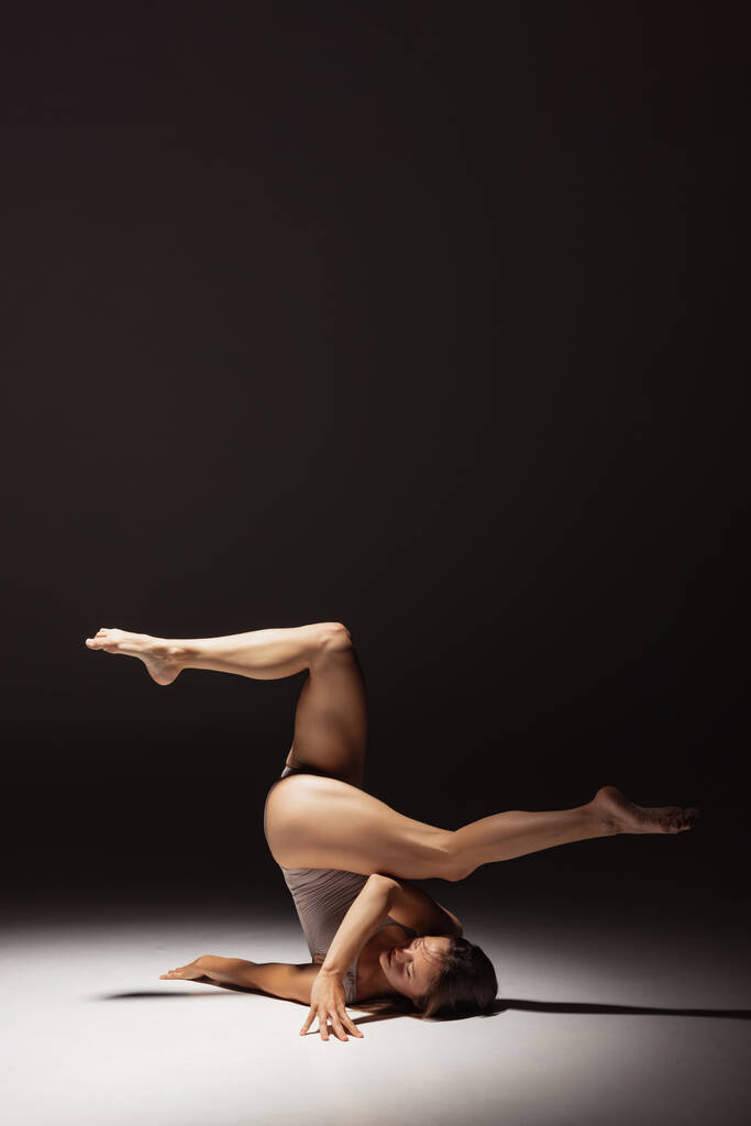 Dynamiczny portret młodego elastycznego tancerza kontemplacyjnego tańczącego na ciemnym tle studia w centrum uwagi. Sztuka, piękno, koncepcja inspiracji. - Zdjęcie, obraz