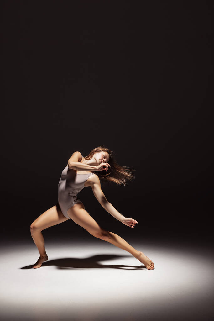 Dynamisch portret van jonge flexibele contemp danser dansen geïsoleerd op donkere studio-achtergrond in de schijnwerpers. Kunst, schoonheid, inspiratie concept. - Foto, afbeelding