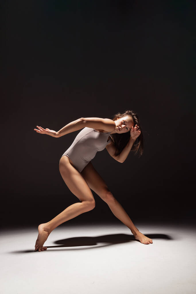 Динамічний портрет молодої гнучкої презирливої танцівниці, що танцює ізольовано на темному студійному фоні в центрі уваги. Мистецтво, краса, концепція натхнення
. - Фото, зображення