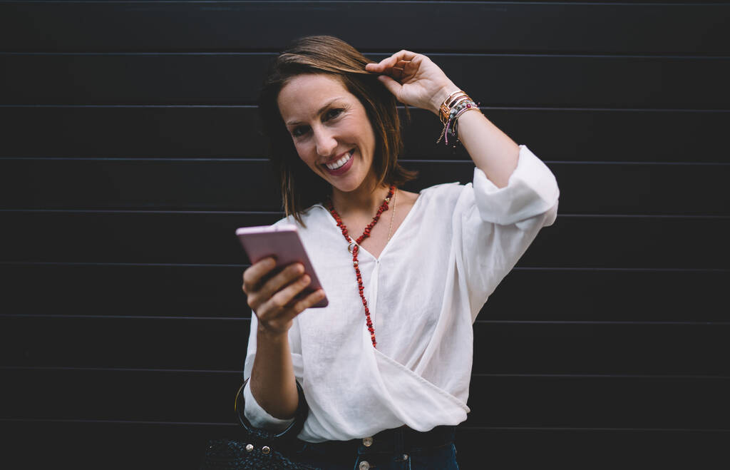 Ritratto di mezza lunghezza di felice blogger donna di 30 anni utilizzando la tecnologia cellulare nell'area pubblicitaria, allegra donna caucasica che sorride alla fotocamera mentre si connette a Internet 4g sul dispositivo smartphone - Foto, immagini