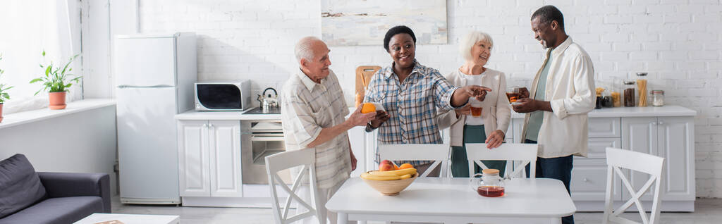 Anziani interrazziali positivi con tè e smartphone nella casa di cura, banner  - Foto, immagini