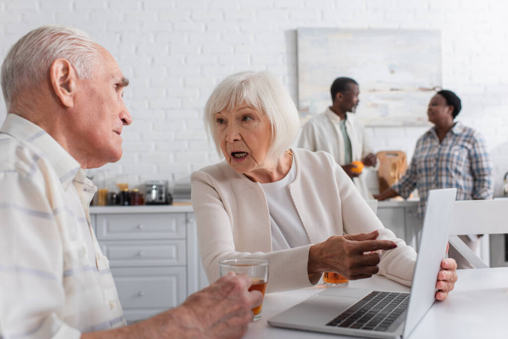 Idős nő a laptopra mutat, közel az idősebb barátjához és teához az idősek otthonában.  - Fotó, kép