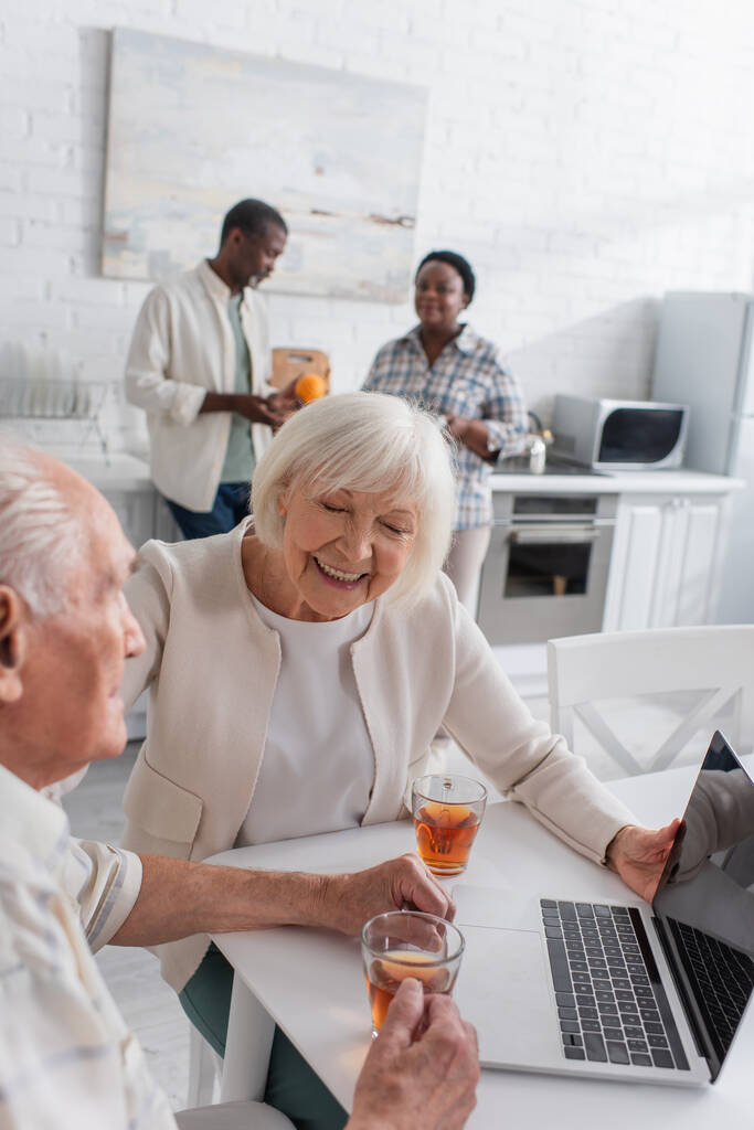 Χαρούμενη γυναίκα κάθεται κοντά ανώτερος φίλος με το τσάι και το laptop στο γηροκομείο  - Φωτογραφία, εικόνα