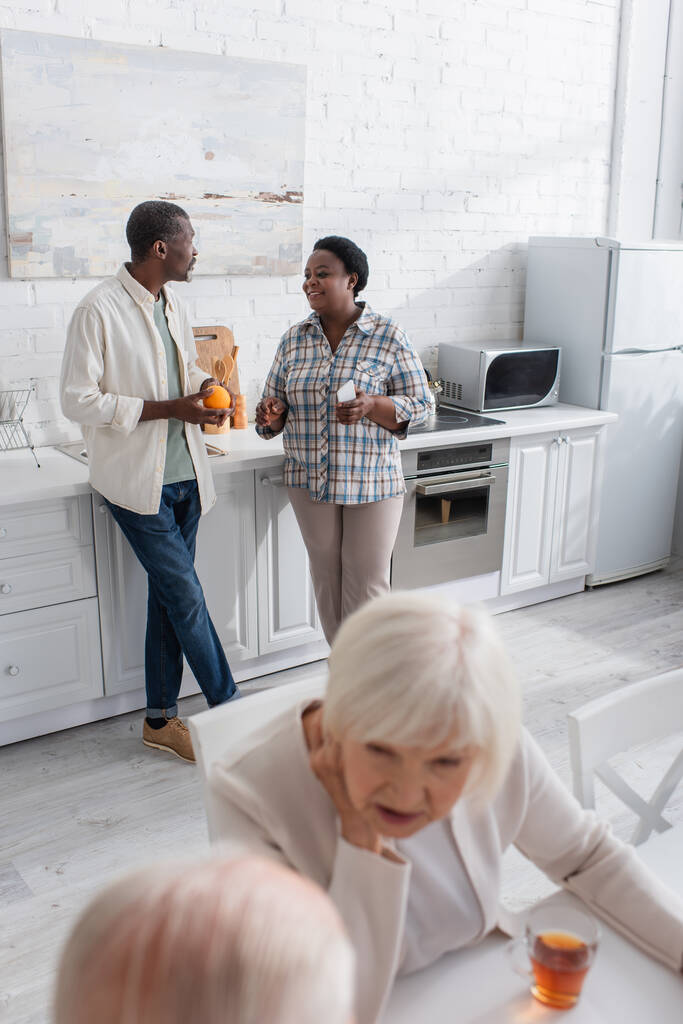 Mosolygó afro-amerikai emberek gyümölcs és okostelefon beszél konyha idősek otthona  - Fotó, kép