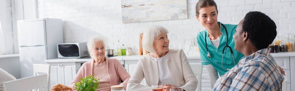 Vidám idős, fajok közötti nők beszélgetnek az ápolónővel az idősek otthonában, transzparens  - Fotó, kép
