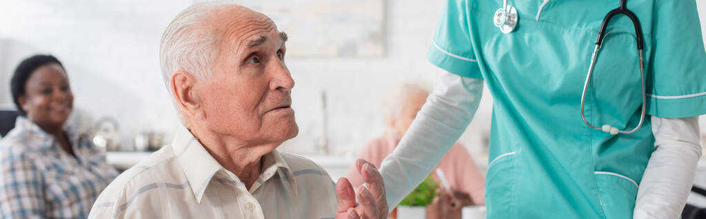 Vanhempi mies puhuu lähellä sairaanhoitaja hoitokodissa, banneri  - Valokuva, kuva