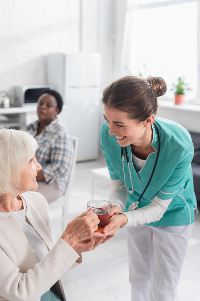 Mosolygó nővér kezében tea mellett beteg idősek otthonában  - Fotó, kép