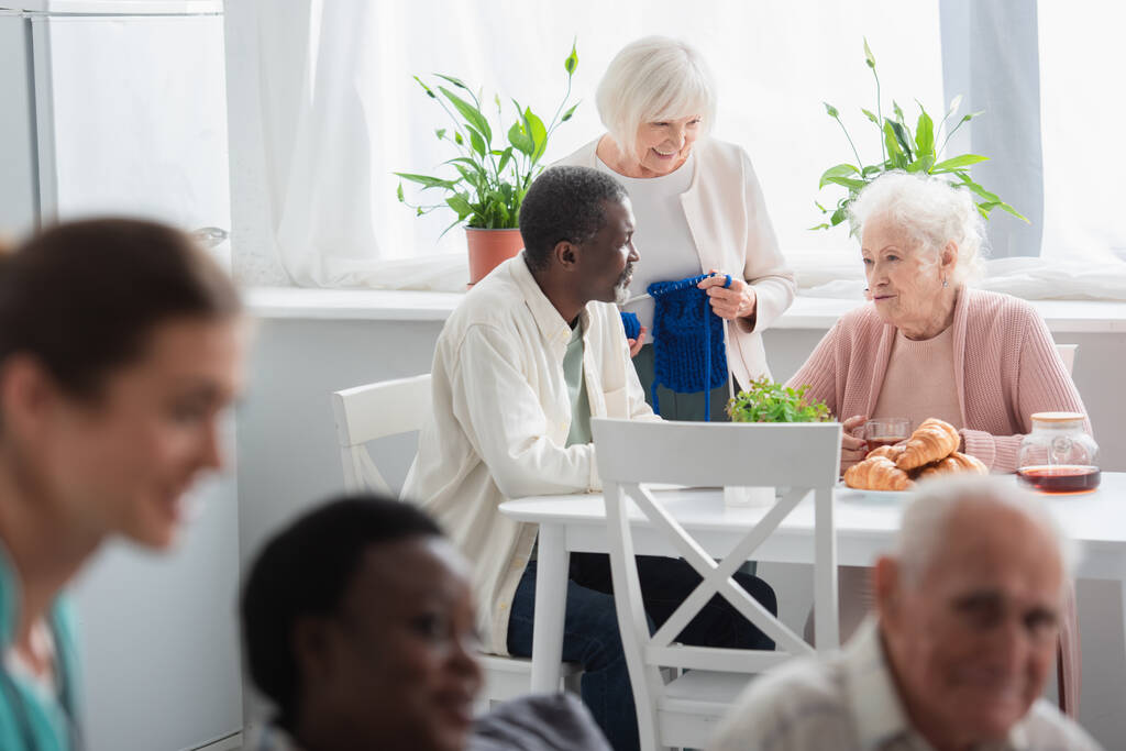 Fonallal és teával mosolygó fajok közötti betegek beszélgetnek az idősek otthonában  - Fotó, kép