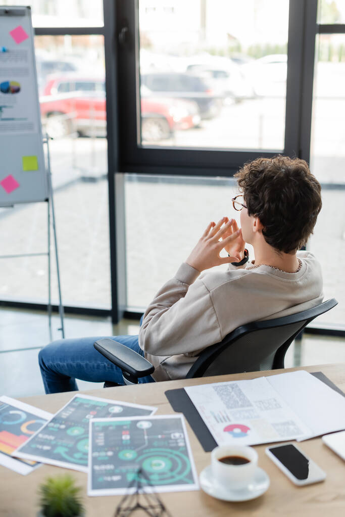 Продвинутый бизнесмен рассматривает размытую флип-карту рядом с документами и кофе в офисе  - Фото, изображение