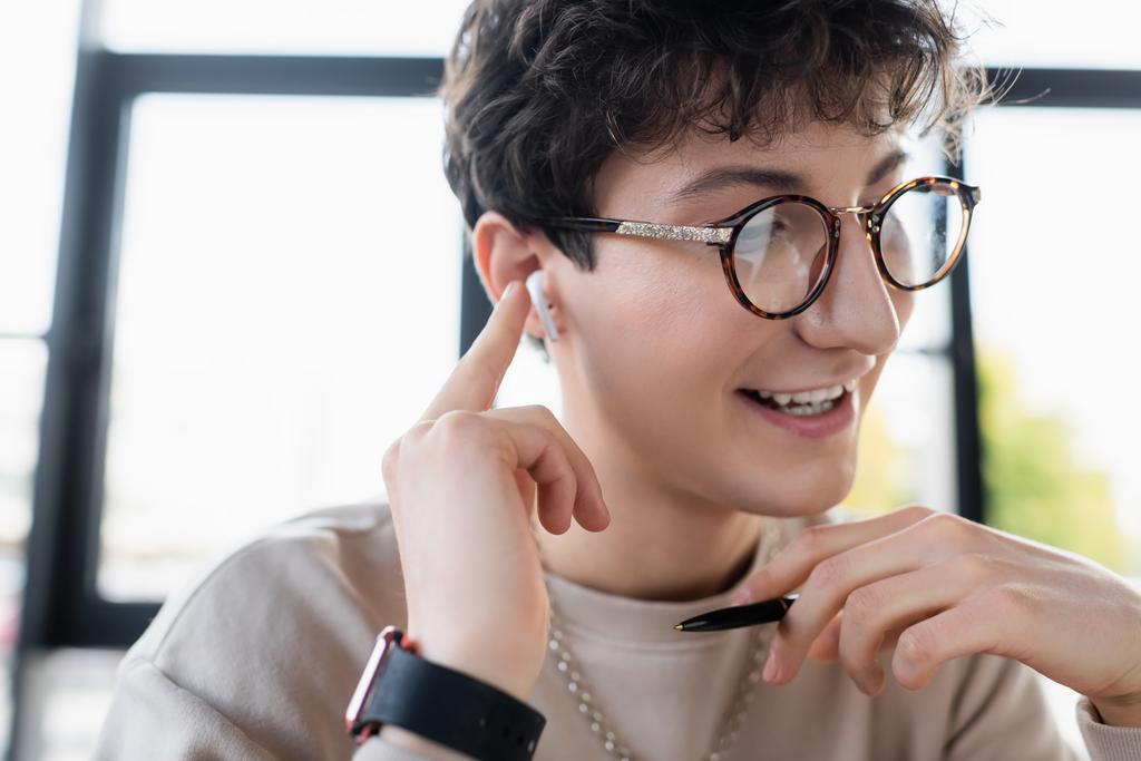 Jonge transgender in bril en oortelefoon met pen in functie   - Foto, afbeelding