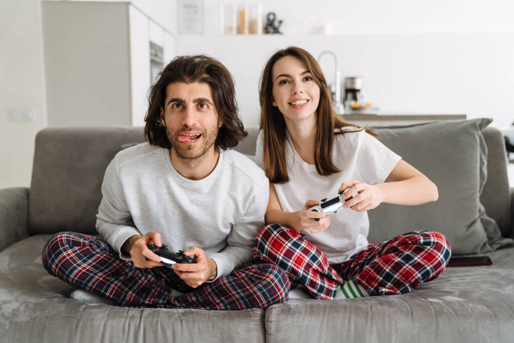 Nuori onnellinen pari tilalla joysticks pelejä tv-ruudulla, kun katsot tv-ruudulla kotona - Valokuva, kuva