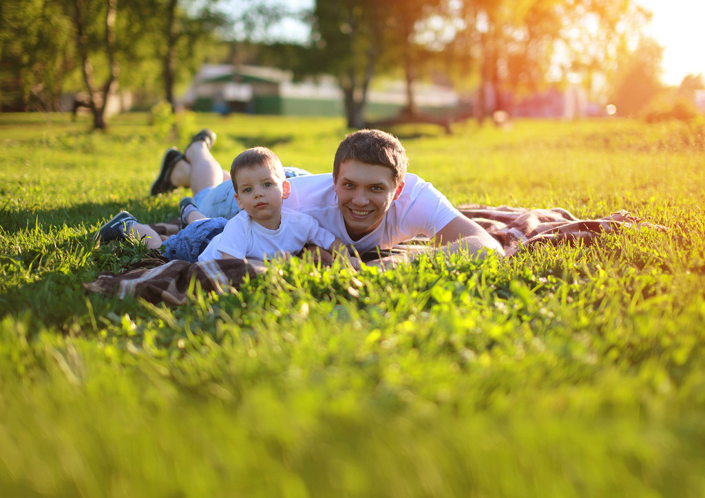 Gelukkig vader en zoon plezier liggen op het gras in de zomerzon - Foto, afbeelding