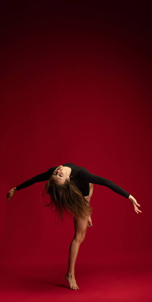 若い柔軟な女の子のスタジオショット,女性の現代舞踊家,暗赤色の背景に隔離されたアクションでバレリーナ.芸術、美、インスピレーションの概念. - 写真・画像
