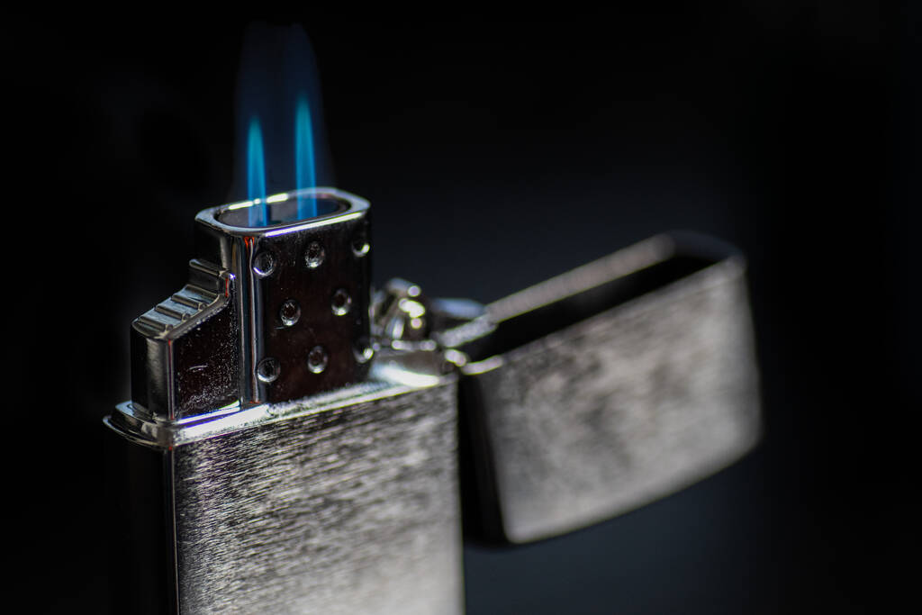 крупним планом відкритий срібний запальничка з блакитним полум'ям на темному тлі
 - Фото, зображення