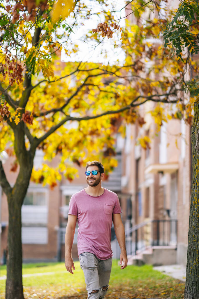 Молодий кавказький стиліст у рожевій сорочці і сонцезахисних окулярах, що ходять по вулиці. - Фото, зображення