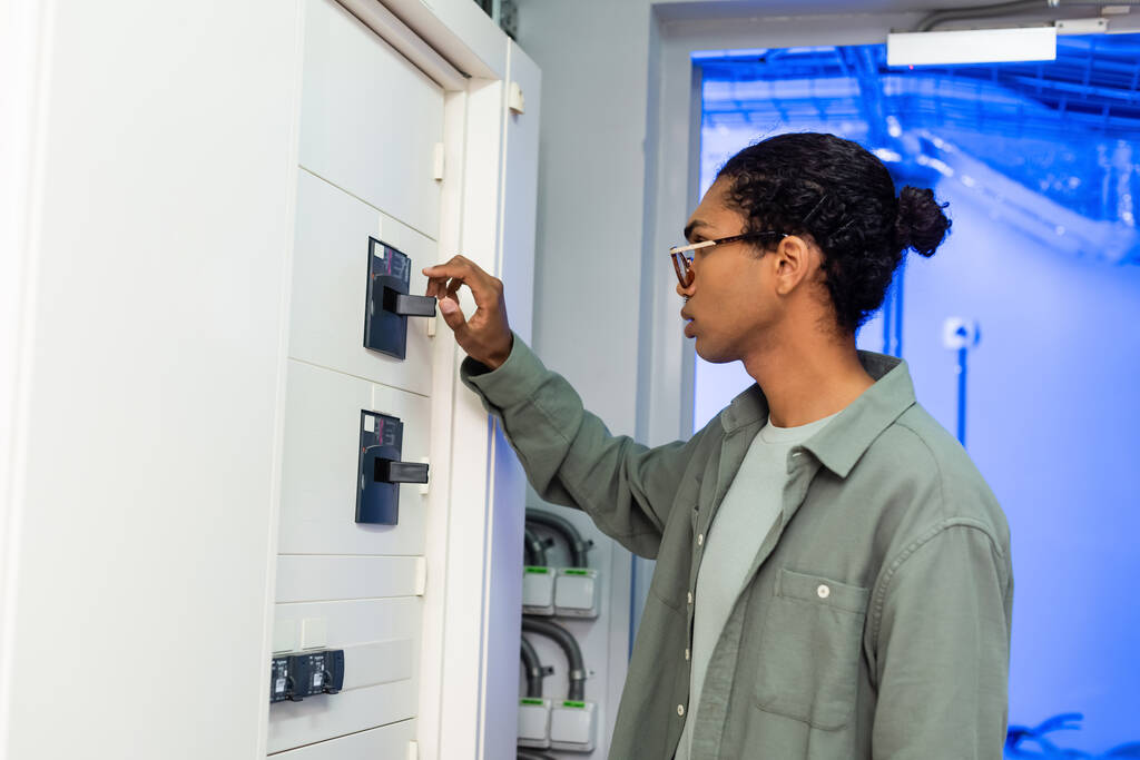 junger afrikanisch-amerikanischer Ingenieur macht Wartung von Schaltanlagen während er im Rechenzentrum arbeitet - Foto, Bild
