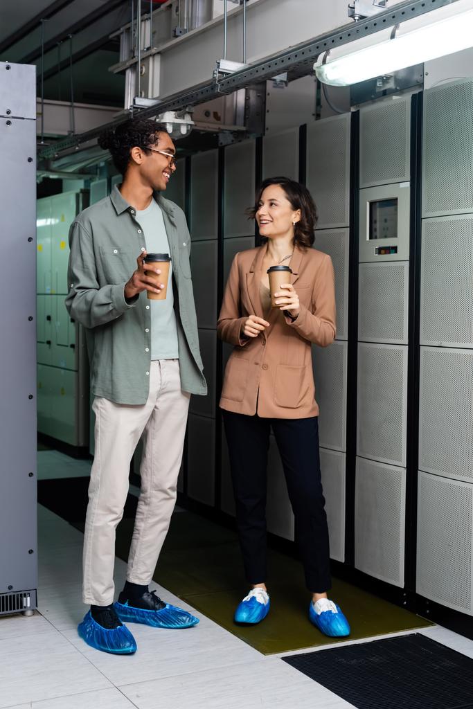 sorridente ingegneri interrazziale in possesso di caffè per andare durante la conversazione in data center - Foto, immagini