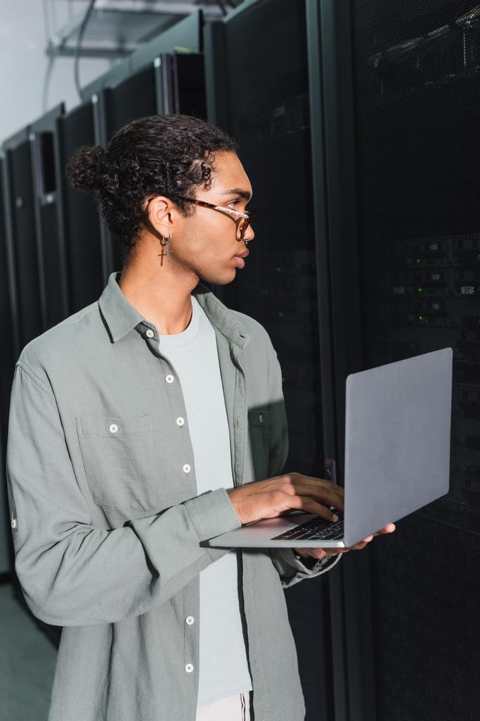 young african american programmer using laptop while working with servers in data center - Photo, Image