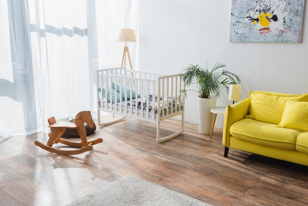 przestronny pokój z żółtą sofą, łóżeczkiem niemowlęcym i koniem - Zdjęcie, obraz