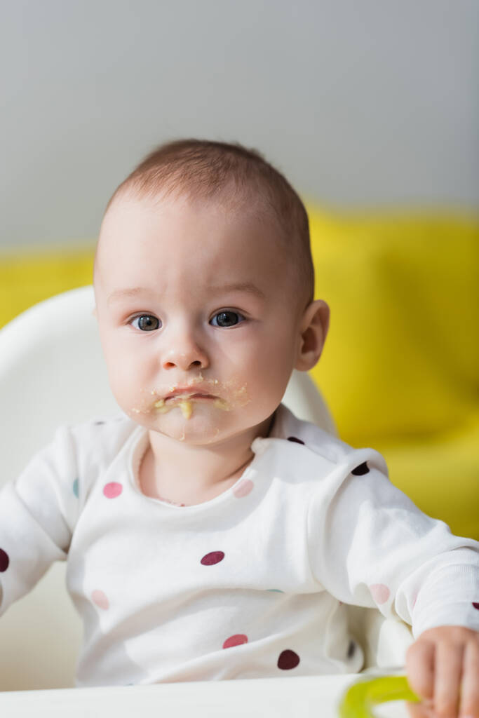 赤ちゃんの椅子に座っている唇に食べ物を持つ幼児 - 写真・画像