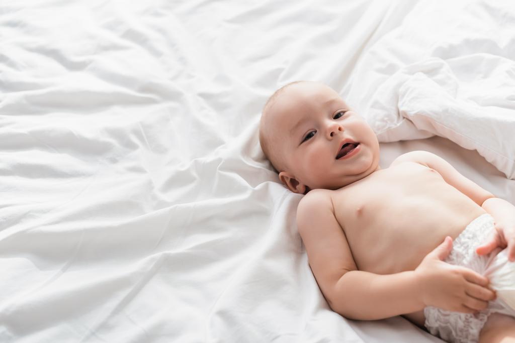 little boy in diapers lying on white bedding and looking at camera - Photo, Image