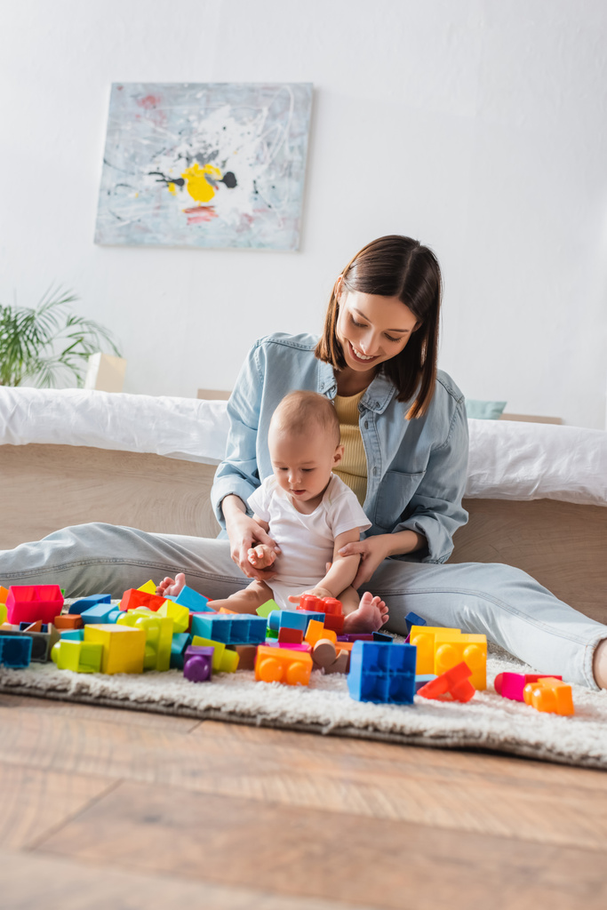 femme heureuse avec tout-petit enfant assis sur le sol dans la chambre et jouer avec les blocs de construction - Photo, image
