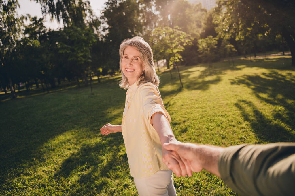 Фото старшей радостной женщины хорошее настроение держать за руку муж следуйте за мной прогулка парк солнечная весна природа на открытом воздухе - Фото, изображение
