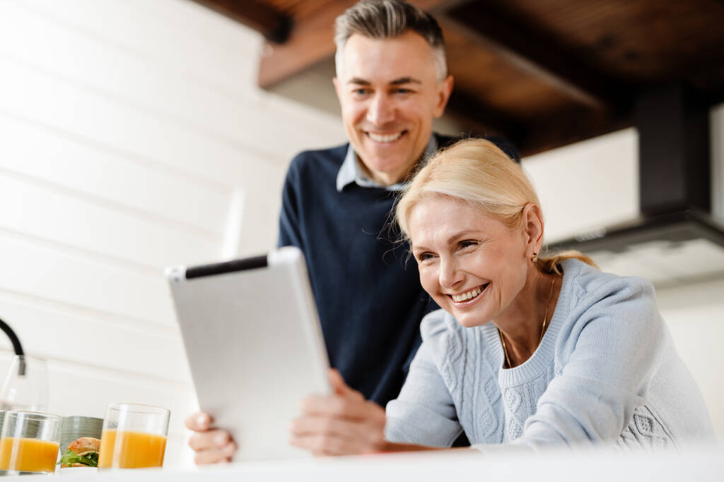 Χαμογελώντας μεσήλικες ζευγάρι σε μια βιντεοκλήση μέσω ψηφιακής tablet από το σπίτι - Φωτογραφία, εικόνα