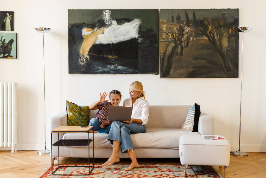 Mãe branca e filha gesticulando e usando celular enquanto sentado no sofá em casa - Foto, Imagem