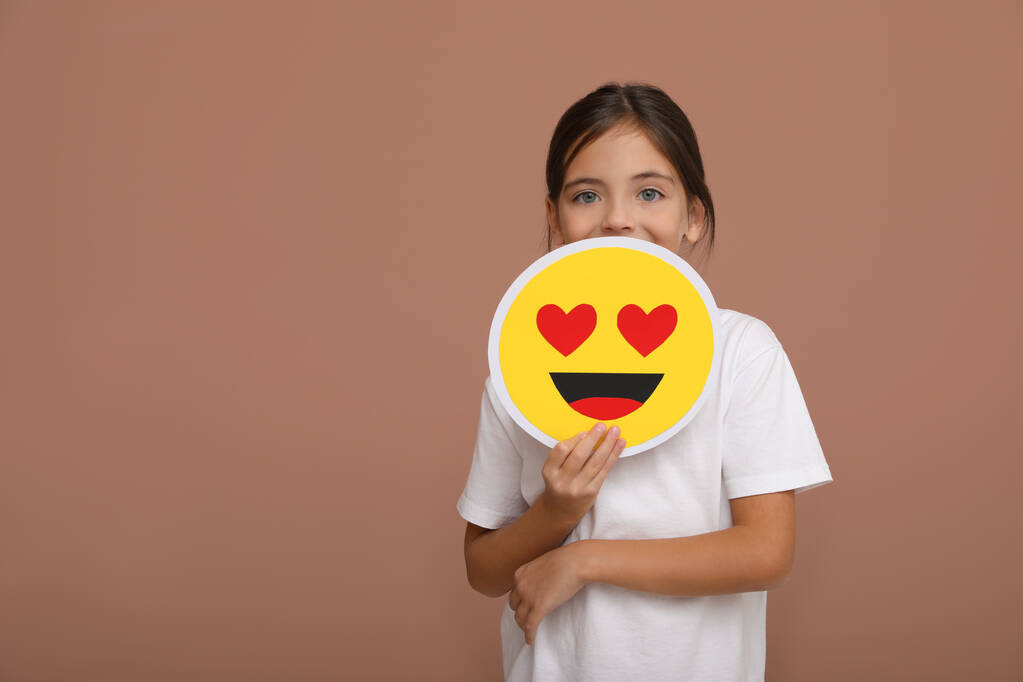 Petite fille tenant visage avec coeur yeux emoji sur fond rose pâle, espace pour le texte - Photo, image
