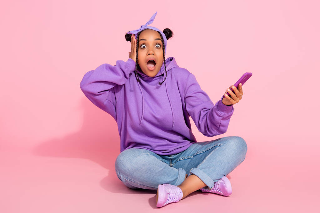 Фото шокованої красивої африканської леді, одягненої в фіолетовий светр булочки рука голова тримає сучасний гаджет ізольований рожевий кольоровий фон
 - Фото, зображення