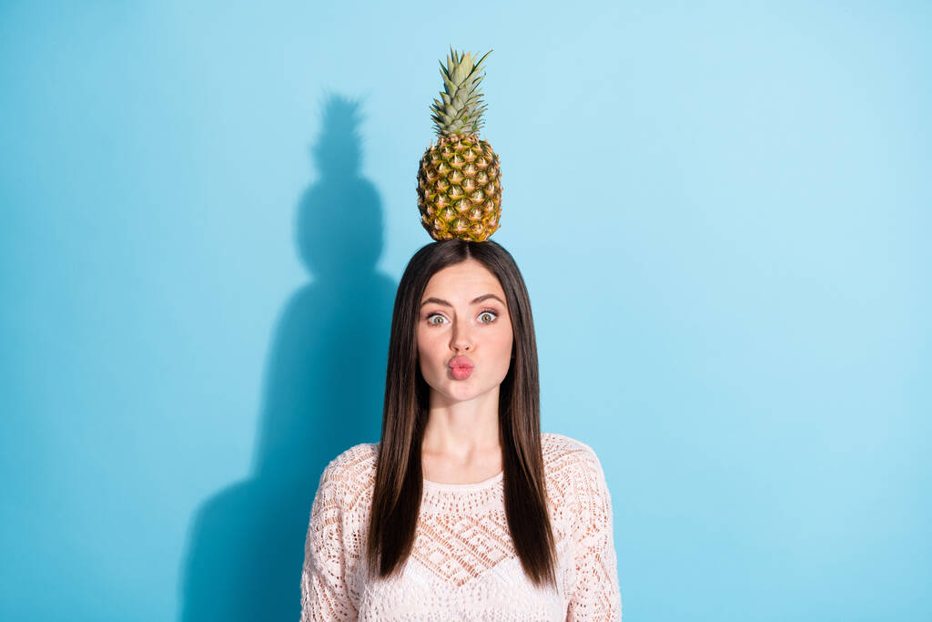 Güzel bir genç kadının fotoğrafı, mavi arka planda izole edilmiş kafaya hava öpücüğü dengesi ananası gönderir. - Fotoğraf, Görsel