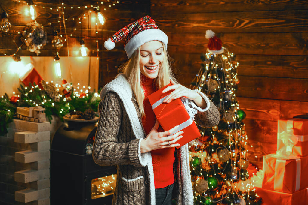 Γυναίκα άνοιξε το χριστουγεννιάτικο δώρο κοντά στο χριστουγεννιάτικο δέντρο. Κορίτσι απολαμβάνουν ζεστή ατμόσφαιρα παραμονή Χριστουγέννων ή νόελ. - Φωτογραφία, εικόνα