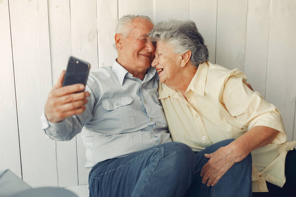 Zarif yaşlı çift evde oturuyor ve telefon kullanıyor. - Fotoğraf, Görsel