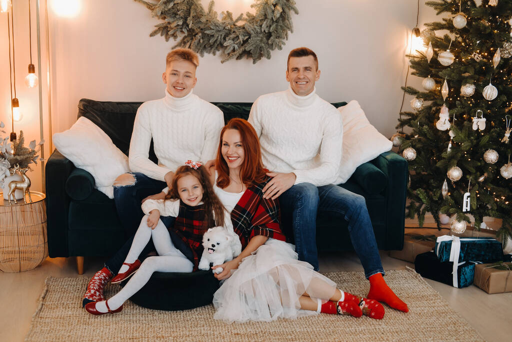Retrato de cerca de una familia feliz sentada en un sofá cerca de un árbol de Navidad celebrando unas vacaciones. - Foto, imagen