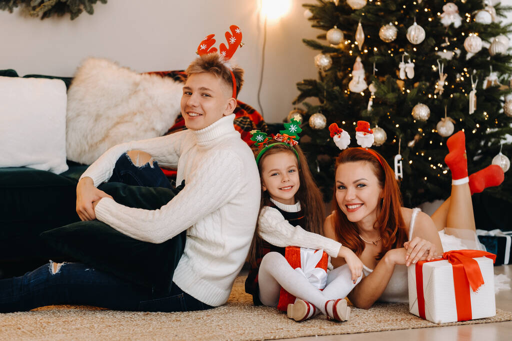 egy boldog család fekszik a ház padlóján szilveszteri ajándékokkal, a karácsonyfa mellett., - Fotó, kép