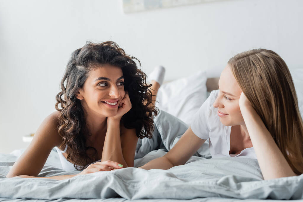 feliz pareja lesbiana mirándose y acostada en la cama - Foto, Imagen