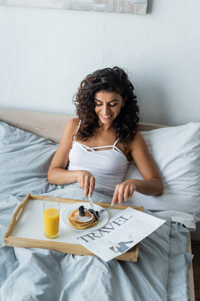 cheerful young woman having pancakes on breakfast in bedroom  - Photo, Image