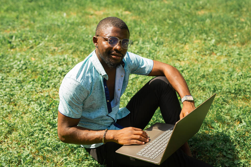 bell'uomo africano che riposa seduto sull'erba nel parco con un portatile - Foto, immagini