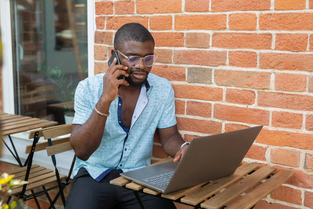 handsome african man working with laptop against brick wall background - Photo, Image