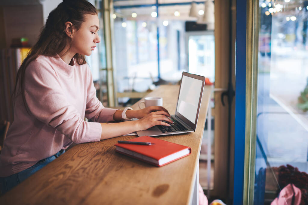 Sivunäkymä nuorten naisten freelancer rento asu selailu kannettava tietokone istuu pöydässä kannettavan työskennellessään projektin kahvilassa - Valokuva, kuva