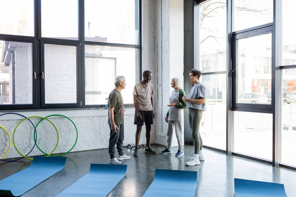 Interrassische Senioren in Sportkleidung unterhalten sich im Fitnessstudio  - Foto, Bild