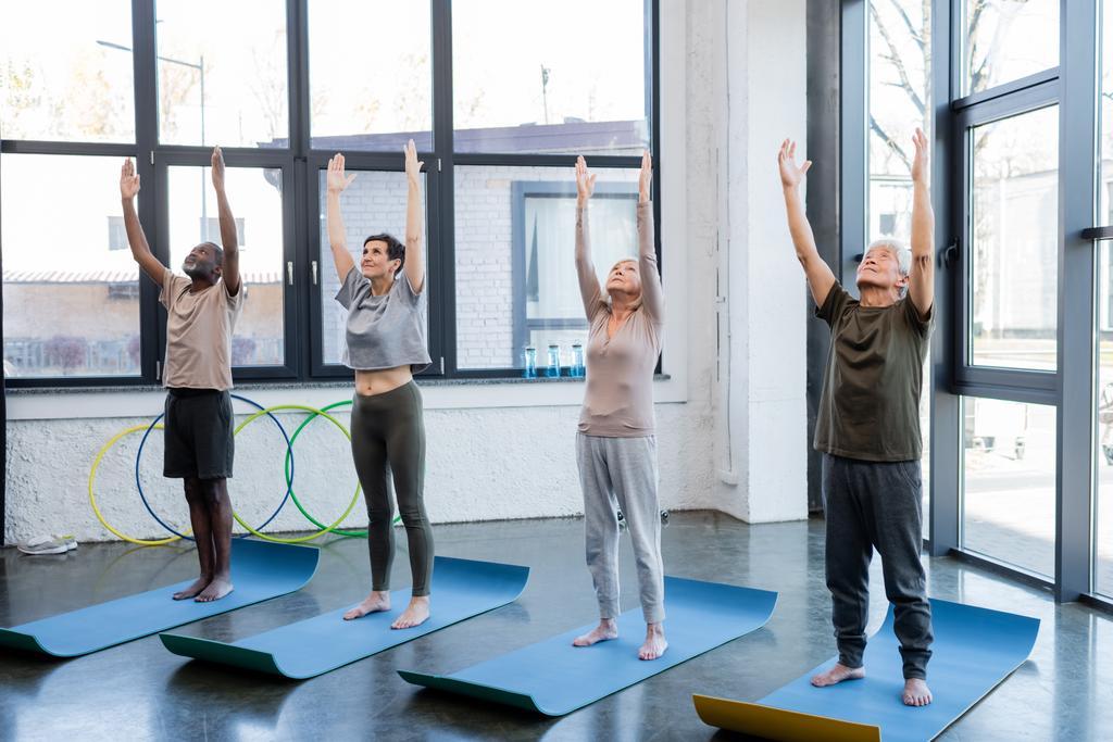 Багатоетнічні літні люди, які піднімають руки під час практики йоги в тренажерному залі
  - Фото, зображення