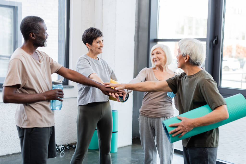 Starší mezirasoví lidé drží fitness rohože a ruce v tělocvičně  - Fotografie, Obrázek
